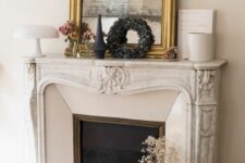 a French fireplace with a decorated mantel, an arrangement of candles, a boho pouf and a mirror in a gilded frame
