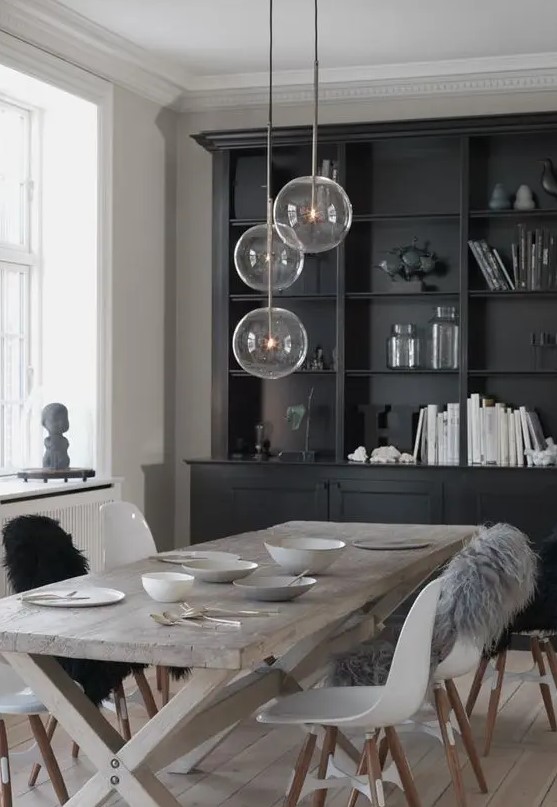 a Nordic dining space with a black storage unit, a reclaimed trestle dining table, white Eames chairs and pendant lamps