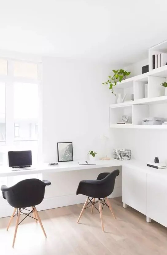 A Nordic light filled working space with open shelves and sleek cabinets, a built in desk and black Eames chairs and potted greenery