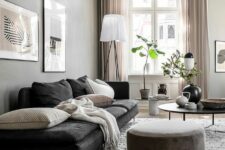a Scandinavian living room with grey walls, a black couch, neutral pillows and a pouf, a round coffee table and potted greenery