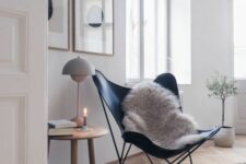 a Scandinavian space with a black leather butterfly chair, a side table with a cool lamp, a mini gallery wall and a glass with candles