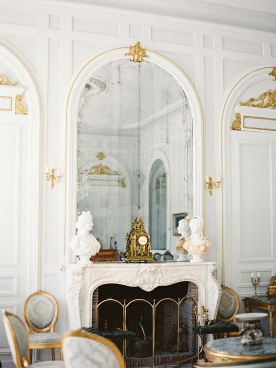 a beautiful French fireplace with decor on the mantel and an arched mirror, gold decor and details here and there