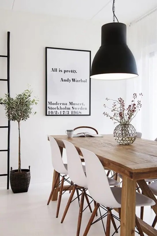 A beautiful Scandinavian dining room with a light stained wooden table, white Eames chairs, a statement black pendant lamp and an artwork