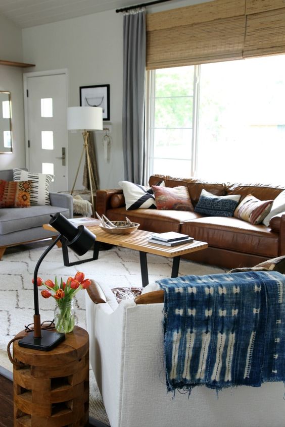a boho living room with a brown leather sofa, a bench as a coffee table, neutral seating furniture, blooms and lamps