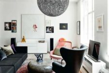 a boho living room with a low black sofa and a black chair, a stone-like coffee table, a pink chair, a black yarn lamp