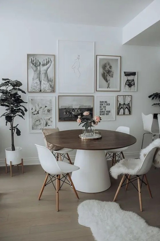 a catchy Scandinavian dining space with a round table, white chairs, a black and white gallery wall and potted plants