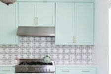 a catchy mint blue kitchen with shaker cabinets, a printed tile backsplash and a checked tile floor, a chic chandelier