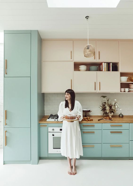 A catchy two tone kitchen with stained and mint blue cabinets, butcherblock countertops and brass handles