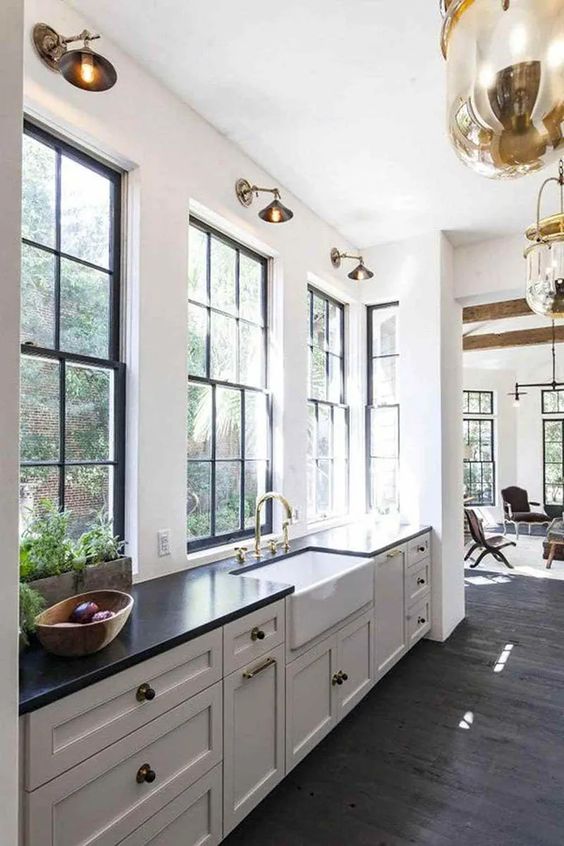 A chic black and white farmhouse kitchen with shaker cabinets, black frame double hung windows, brass knobs and sconces