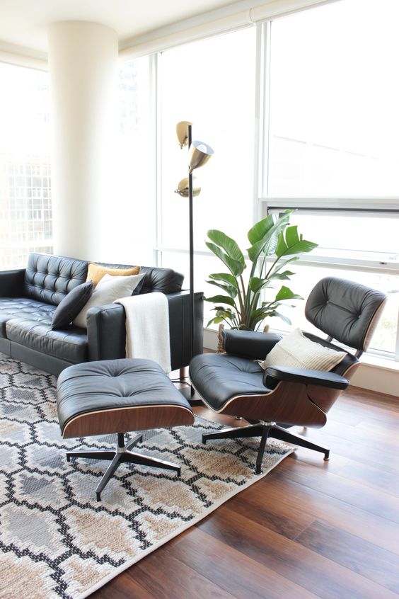 A chic mid century modern living room with a black leather sofa and an Eames lounger and ottoman, a printed rug, a potted plant