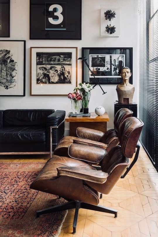 A chic mid century modern living room with a black leather sofa, brown Eames loungers, a black and white gallery wall