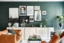 a chic mid-century modern living room with a dark green accent wall, an amber leather sofa and a butterfly chair, a coffee table and a gallery wall
