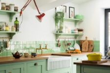 a chic mint green kitchen with shaker cabinets, butcherblock countertops, open shelves and a red sconce