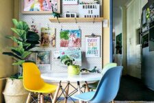 a colorful dining space with a pegboard wall with bright artwork, a round table, colorful Eames chairs, a bright printed rug