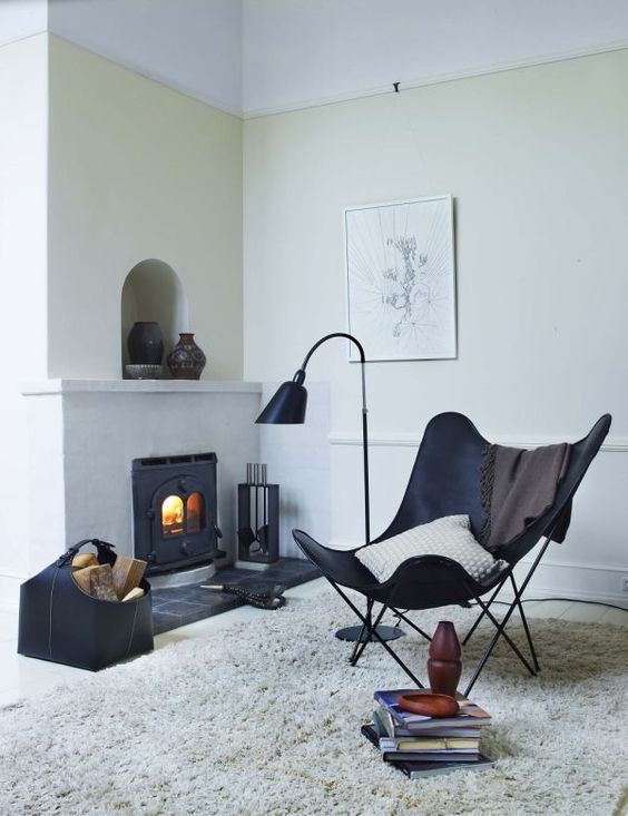 a contrasting nook with a hearth, a black leather butterfly chair, a leather basket with wood, vases and a catchy floor lamp