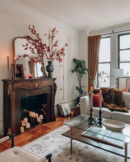 A cozy earthy colored living room with a French fireplace with a stained mantel, a tiered coffee table, a white sofa and a neutral rug plus candles