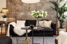 a cozy living room with a black sofa and neutral pillows, a chair, a woven pouf, a side table and a potted plant