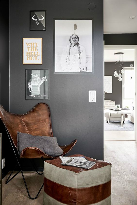 a cozy nook with a brown leather butterfly chair, a matching striped pouf, a gallery wall and a grey pillow