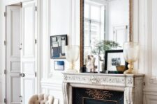 a fab neutral living room with a French fireplace, neutral chairs, an oversized mirror in a chic frame and some decor on the mantel