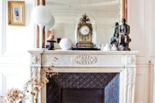 a fabulous French fireplace with an ornated white mantel, an oversized mirror and some vintage decor on the mantel