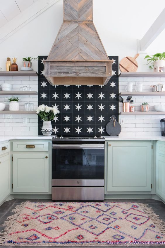 A farmhouse kitchen with mint lower cabinets, open shelves, a white tile backsplash, a reclaimed wood hood