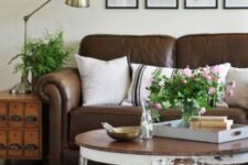 a farmhouse living room with a brown leather sofa, a shabby chic coffee table, a file cabinet, greenery and blooms and a gallery wall