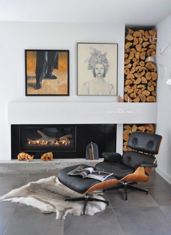 A fireplace nook with a built in fireplace, firewood storage, a black Eames lounger and ottoman, a rug and a mini gallery wall