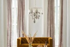 a glam living room with a chandelier, a mustard velvet sofa and blush velvet curtains create a gorgeous ambience