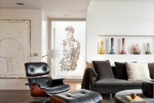 a gorgeous living room with a black sofa, a black Eames lounger, a round coffee table, a niche with vases and lots of art