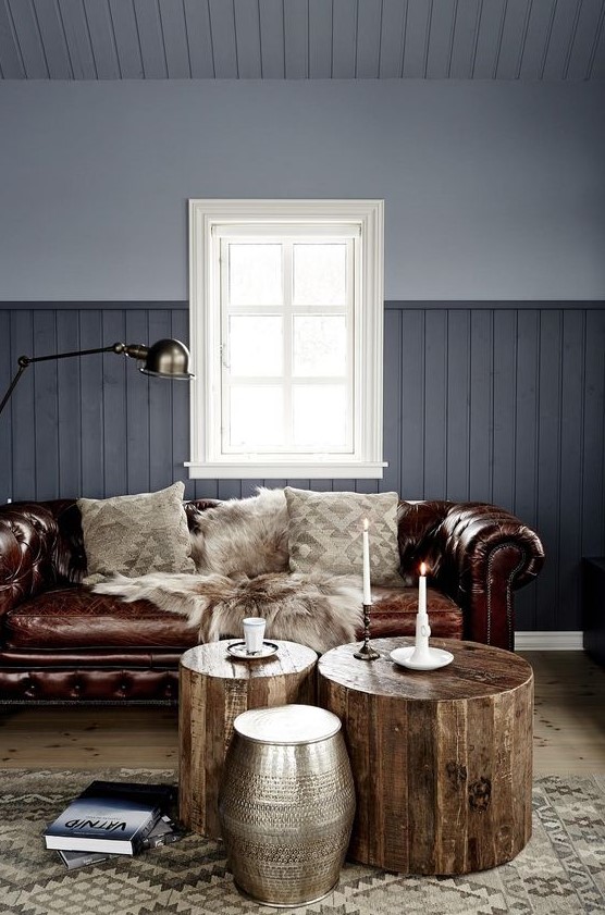 a grey living room with a brown leather Chesterfield sofa, wooden stools and a metal one, candles and a lamp