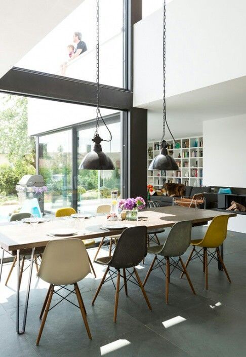 A light filled dining space with a long dining table, colorful Eames chairs, black pendant lamps over the table