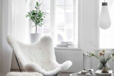 a light-filled living room with arched windows, a white faux fur butterfly chair, a faux fur stool and a glass coffee table