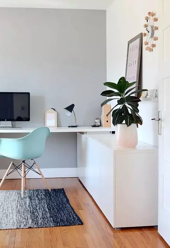 A lovely Scandinavian home office with a sleek storage unit and a built in desk, a mint blue Eames chair, potted greenery and a cool clock