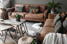 a lovely boho living room with grey walls, brown sofas and grey pillows, hairpin leg tables, potted greenery and a jute rug on the wall