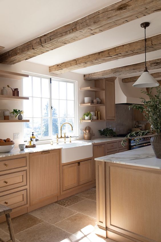 a lovely earthy modern kitchen with light-stained lower cabinets and a kitchen island, rough wooden beams, open shelves