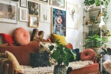 a maximalist living room with a colorful gallery wlal, a rust-colored velvet vintage sofa, a round table and potted plants