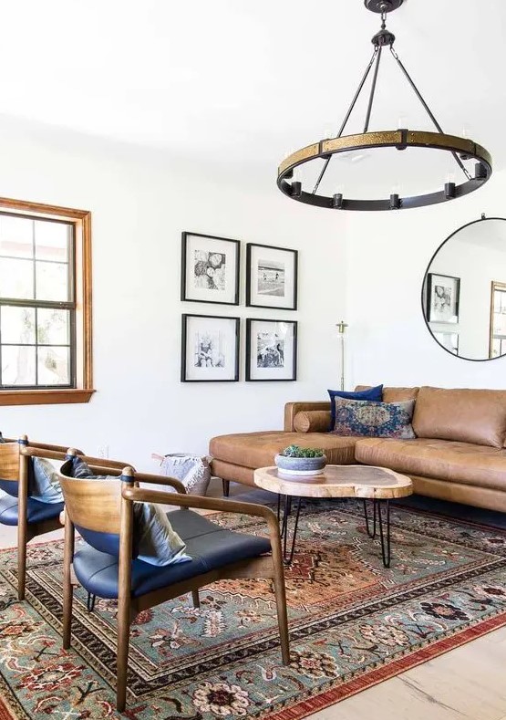 A mid century modern living room with a brown leather sectional, a round coffee table, black chairs, a boho printed rug