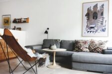 a mid-century modern living room with a grey sectional, a brown leather butterfly chair, a leather pouf and printed pillows