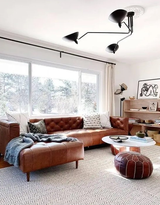 A mid century modern neutral living room with a brown leather corner sofa and matching Moroccan poufs