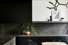 a minimalist black kitchen with flat panel cabinets, grey soapstone countertops and a backsplash, a white hood and a soapstone kitchen island
