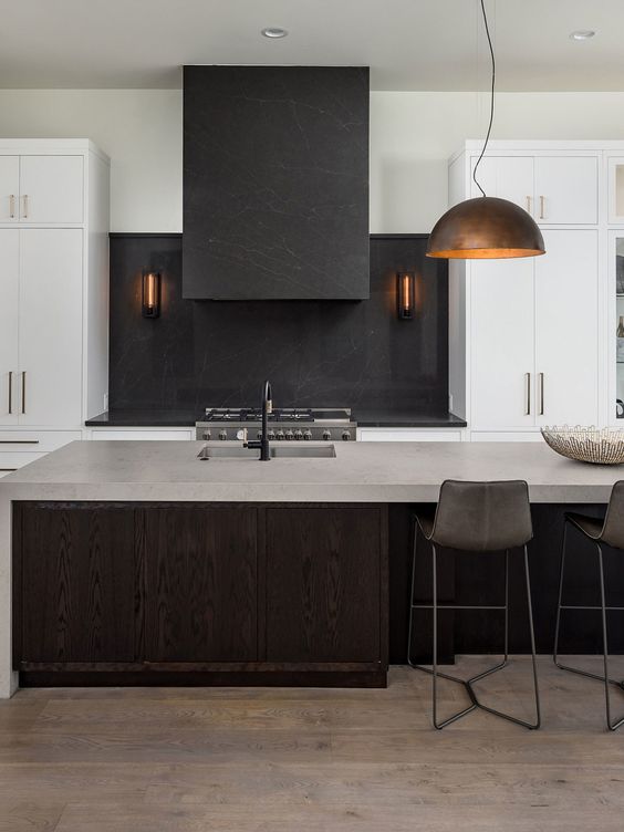 A minimalist kitchen with white cabinets and a dark stained kitchen island, black soapstone countertops and a backsplash and a concrete countertop