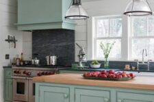a mint blue kitchen with shaker style cabinets, black soapstone countertops and a backsplash, a butcherblock countertop and cool pendant lamps