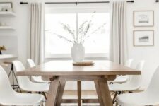 a modern Scandi dining room with a stained trestle dining table, white Eames chairs, a printed rug, a vase with greenery