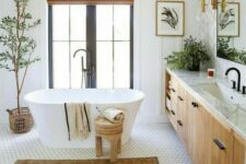 a modern earthy bathroom with hex tiles, an oval tub, a printed rug, a large vanity, black fixtures and potted plants