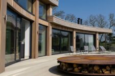 a modern outdoor space with limed oak millboard decking, grey chairs, a firepit with firewood