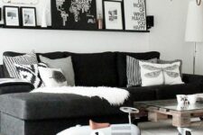 a monochromatic Scandinavian living room with a black sectional, an industrial coffee table, a black ledge with a gallery wall