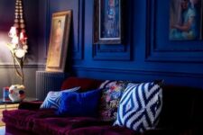 a moody cobalt blue space is made outstanding with a plum-colored velvet sofa that contrasts the walls a lot