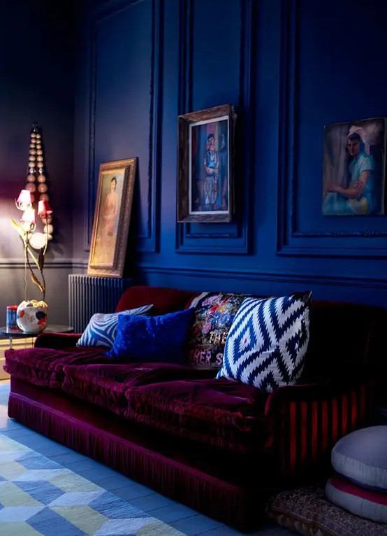 a moody cobalt blue space is made outstanding with a plum-colored velvet sofa that contrasts the walls a lot