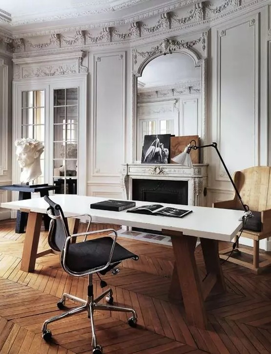 A refined and chic Parisian inspired home office with molding, a French fireplace, a stained chair, a black table, a large desk and a cool lamp