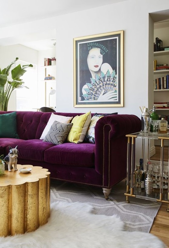 A refined and glam living room in neutrals with a built in bookcase, a purple sofa, a gold table and an acrylic home bar